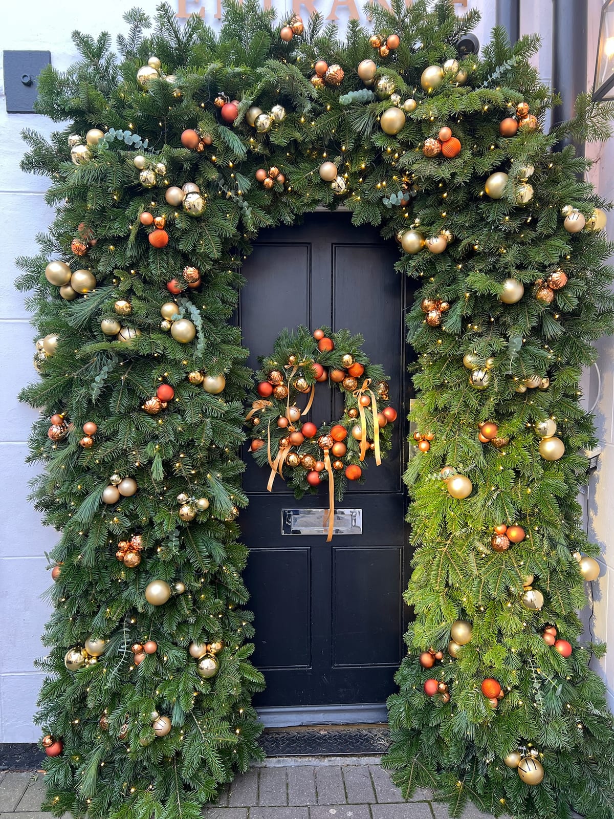 Front door arch dressed with lit garland, gold and copper baubles, and a matching wreath.