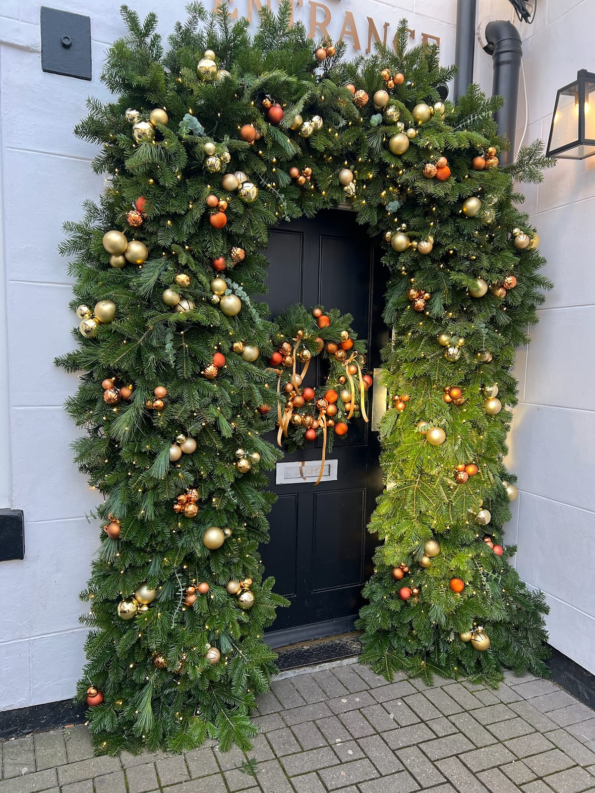 Wider view of a doorway arch dressed in lit garland with gold and copper baubles.