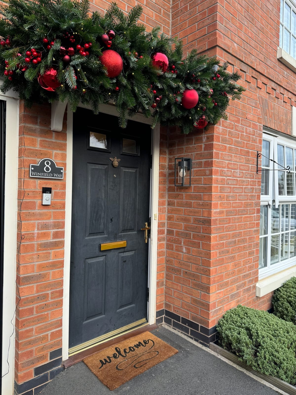 Garland with red baubles and berries fitted above a front door.