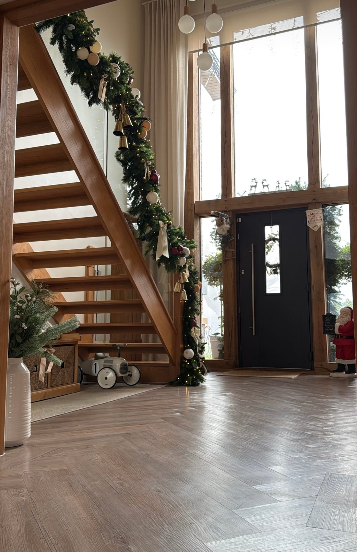 Oak staircase and entrance hall dressed with lit garland, brass bells and ribbon.