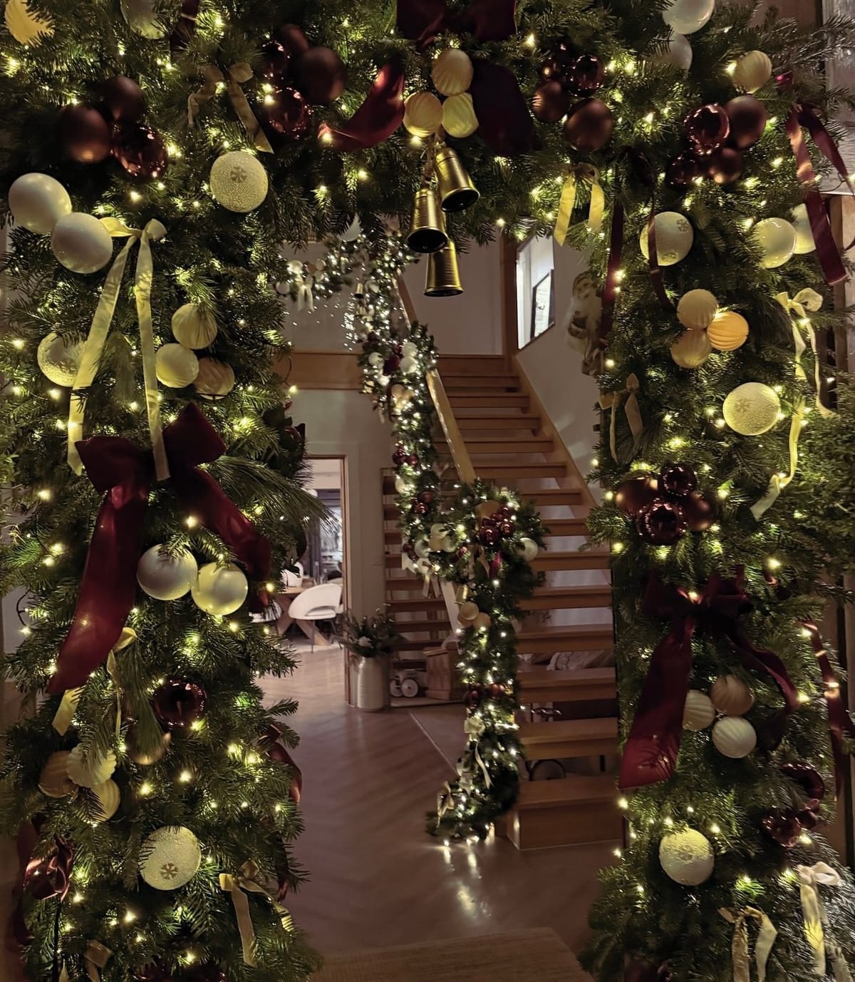 Lit garland arch in burgundy, cream and gold framing an entrance hall, looking through to a dressed oak staircase.