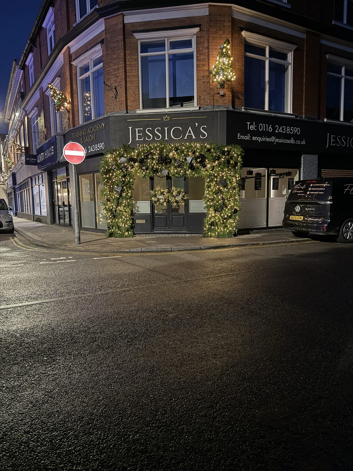 Corner shopfront at night with a lit garland arch in green, gold and black framing the entrance.