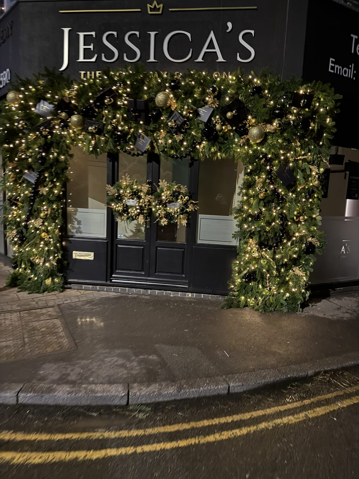 Close view of a shopfront doorway arch dressed in lit garland with gold and black baubles.