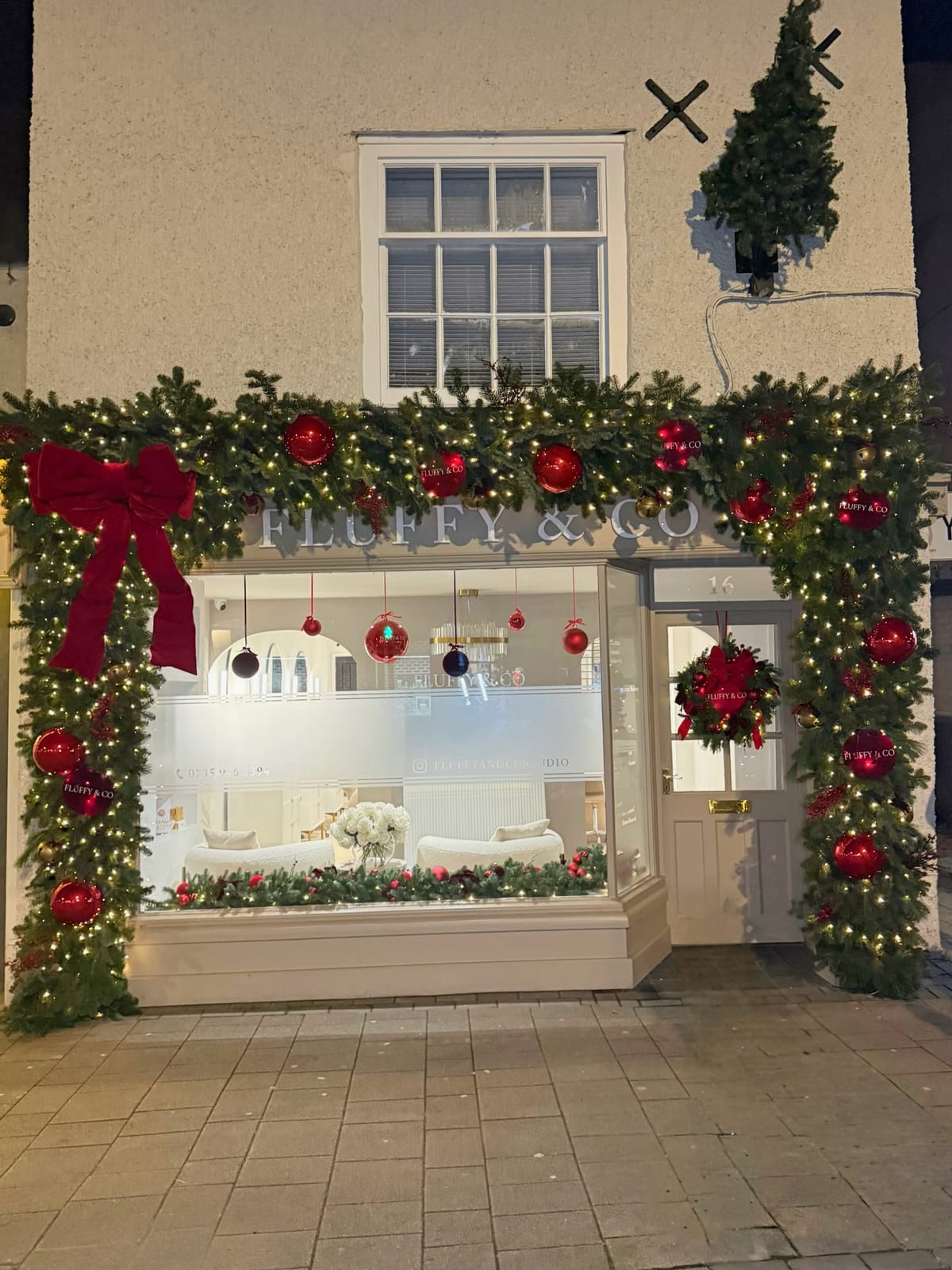 Shopfront framed with lit Christmas garland, red baubles and a large red velvet bow.