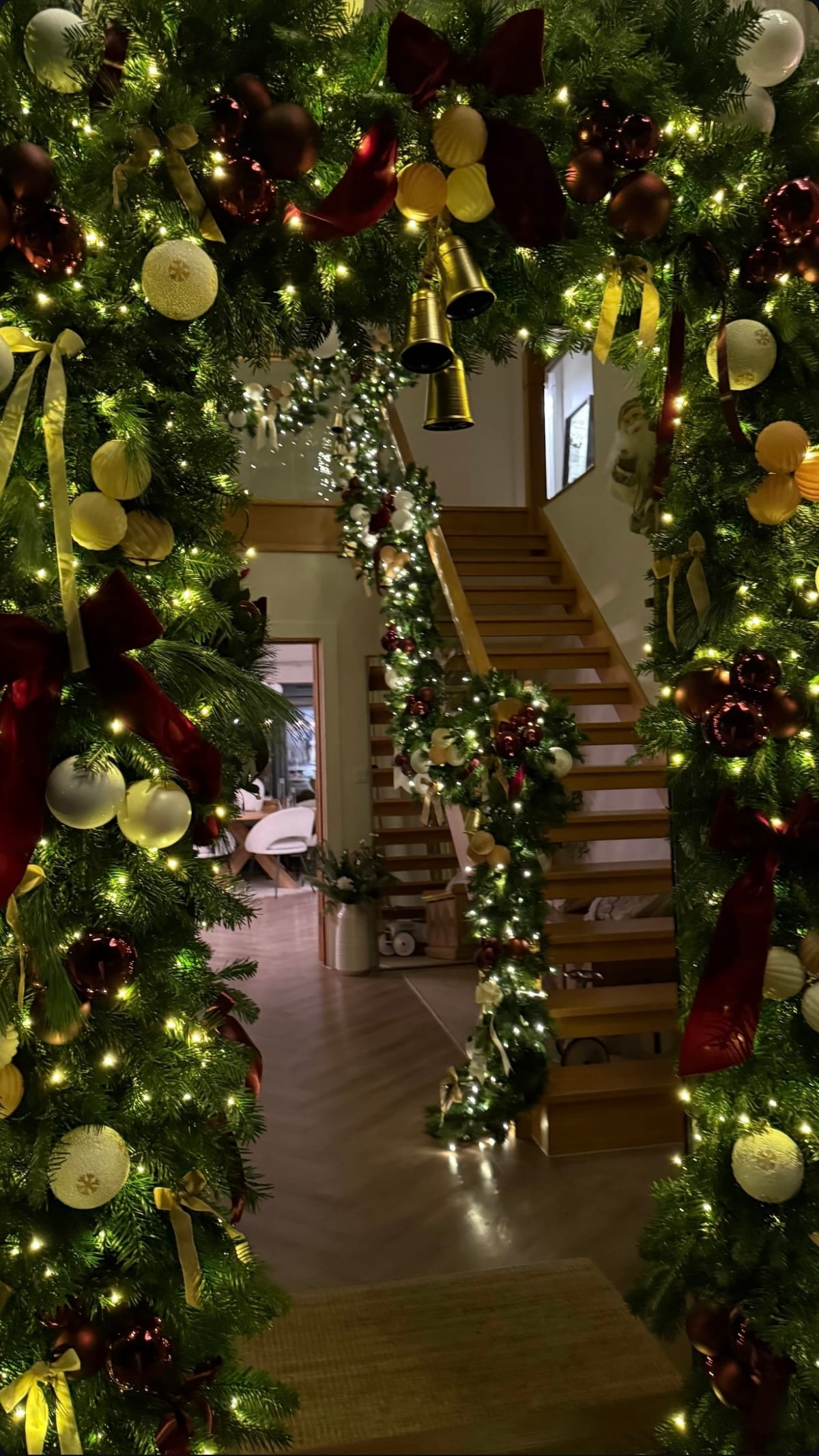 Lit doorway arch dressed with garland, brass bells and velvet ribbon, looking through to a decorated staircase.