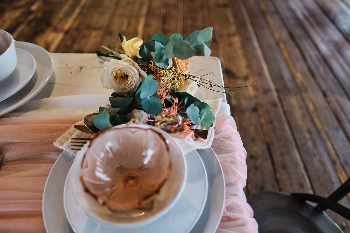 Table place setting with a low arrangement of peach roses and eucalyptus beside a dessert plate and blush ribbon.