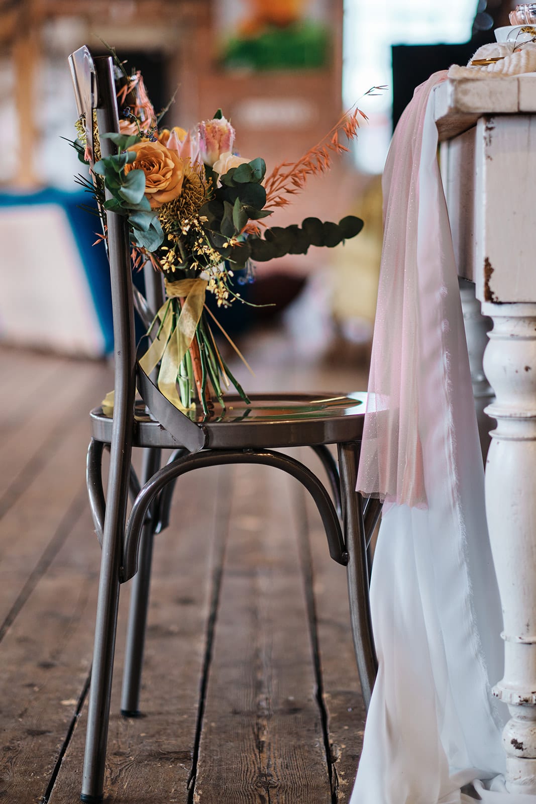 Bridal bouquet of peach and cream roses with eucalyptus and blush ribbon, resting on a wooden chair.