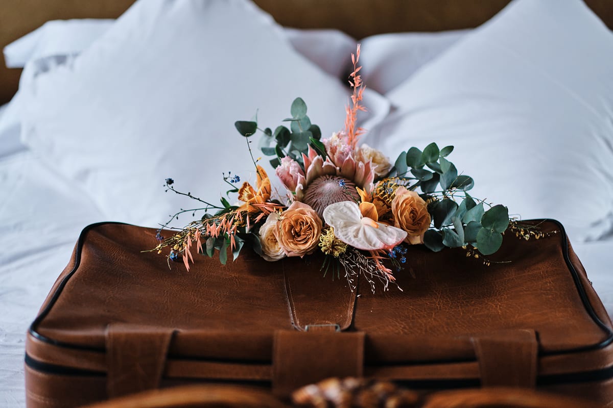Bouquet of peach roses and eucalyptus laid on a leather case on white bedding.