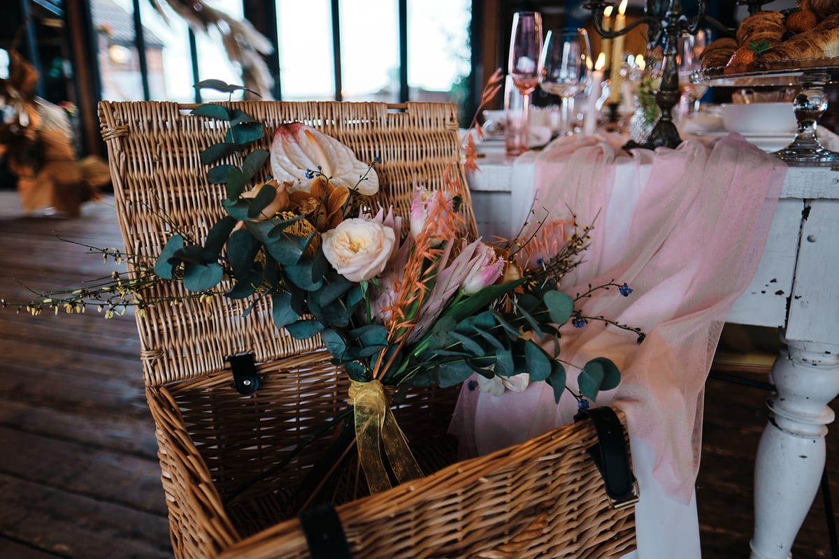Wicker basket filled with peach and cream flowers and trailing blush ribbon.