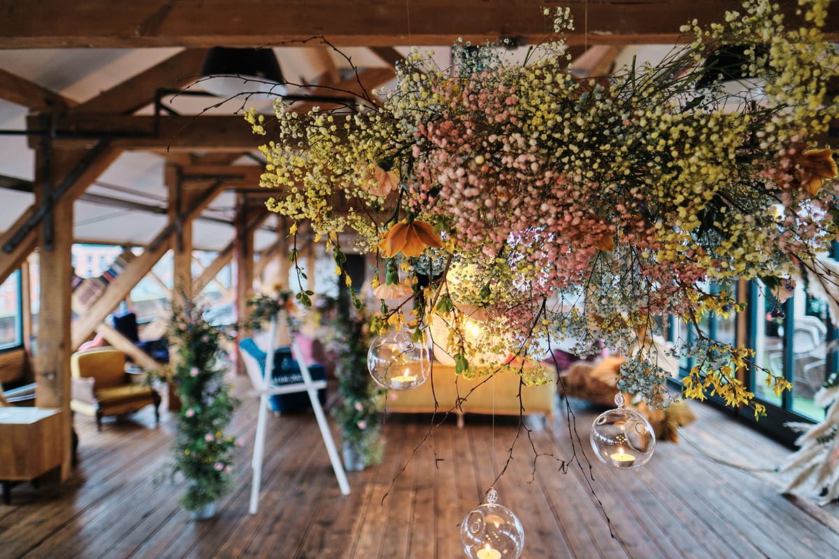 Suspended installation of fine white flowers and foliage above a barn reception space.