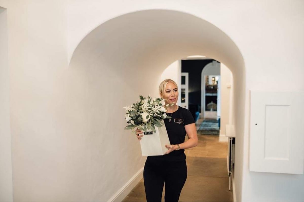 Florist carrying a bouquet of white roses and foliage through a panelled hallway.