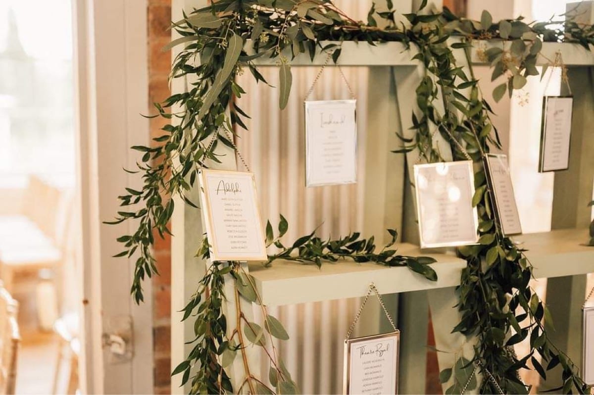 Painted shelving dressed with trailing eucalyptus and hanging framed table cards.