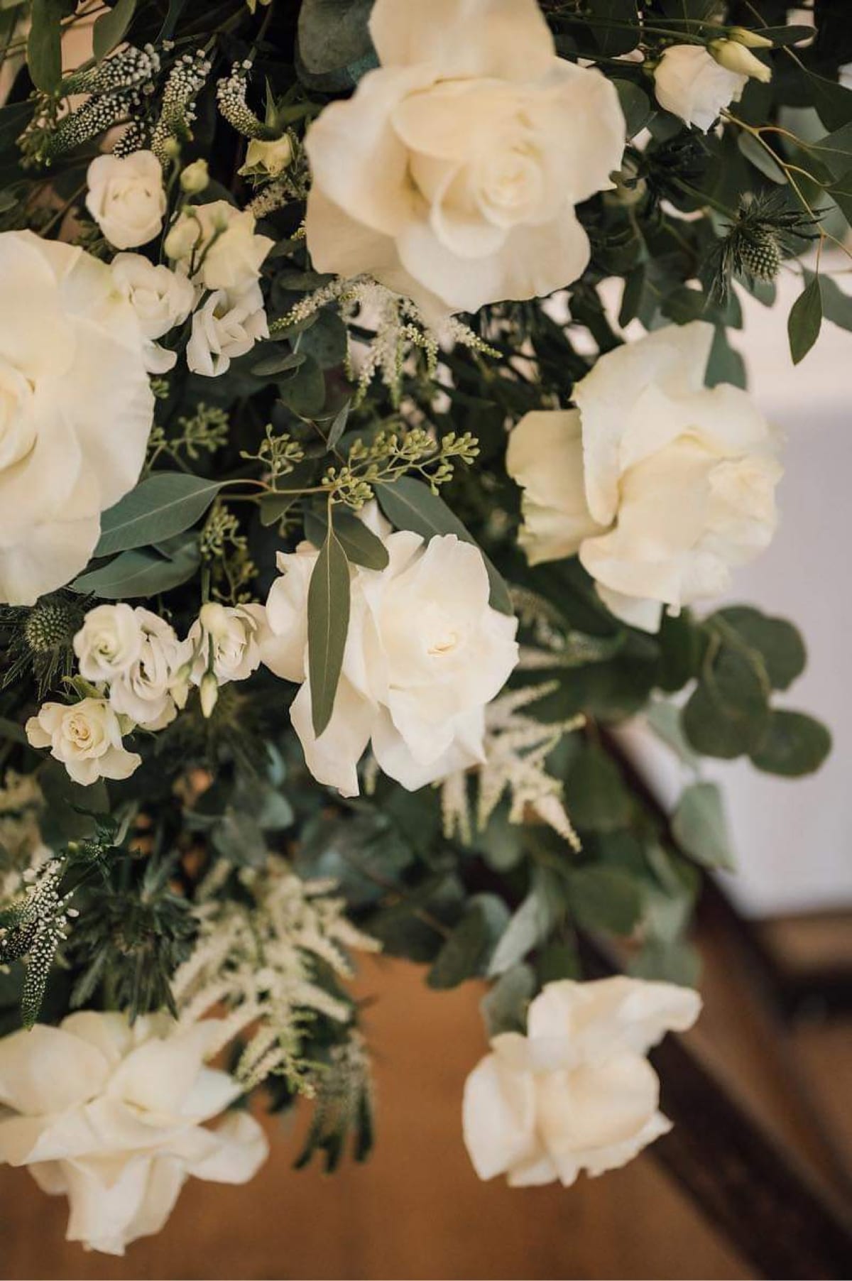 Close view of white roses and eucalyptus mounted on a dark ceremony structure.
