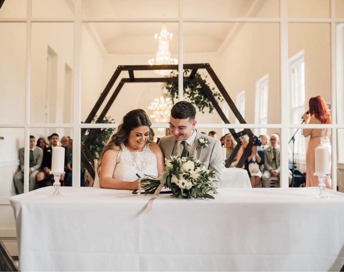 Couple seated at a table beneath a dark arch dressed with white flowers.