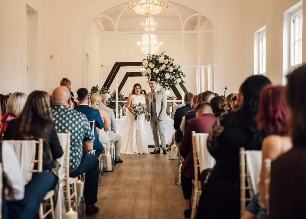 Ceremony in progress in a light panelled room, with guests seated either side of the aisle.