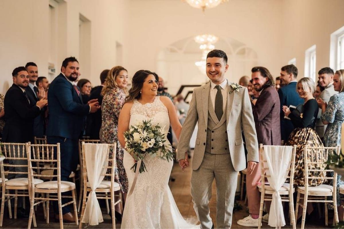 Couple walking through their guests in a panelled reception room.