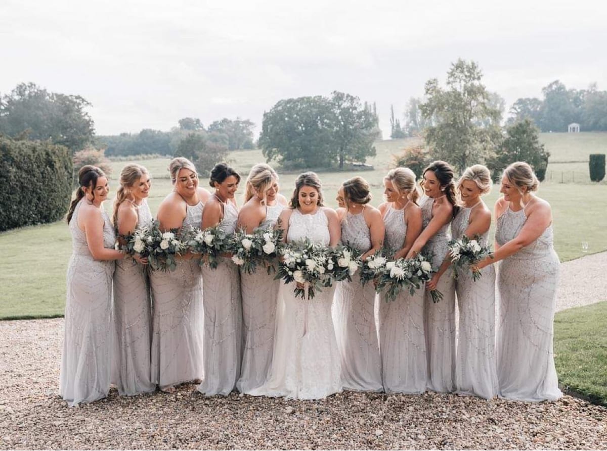 Bridesmaids outdoors holding bouquets of white roses and foliage.
