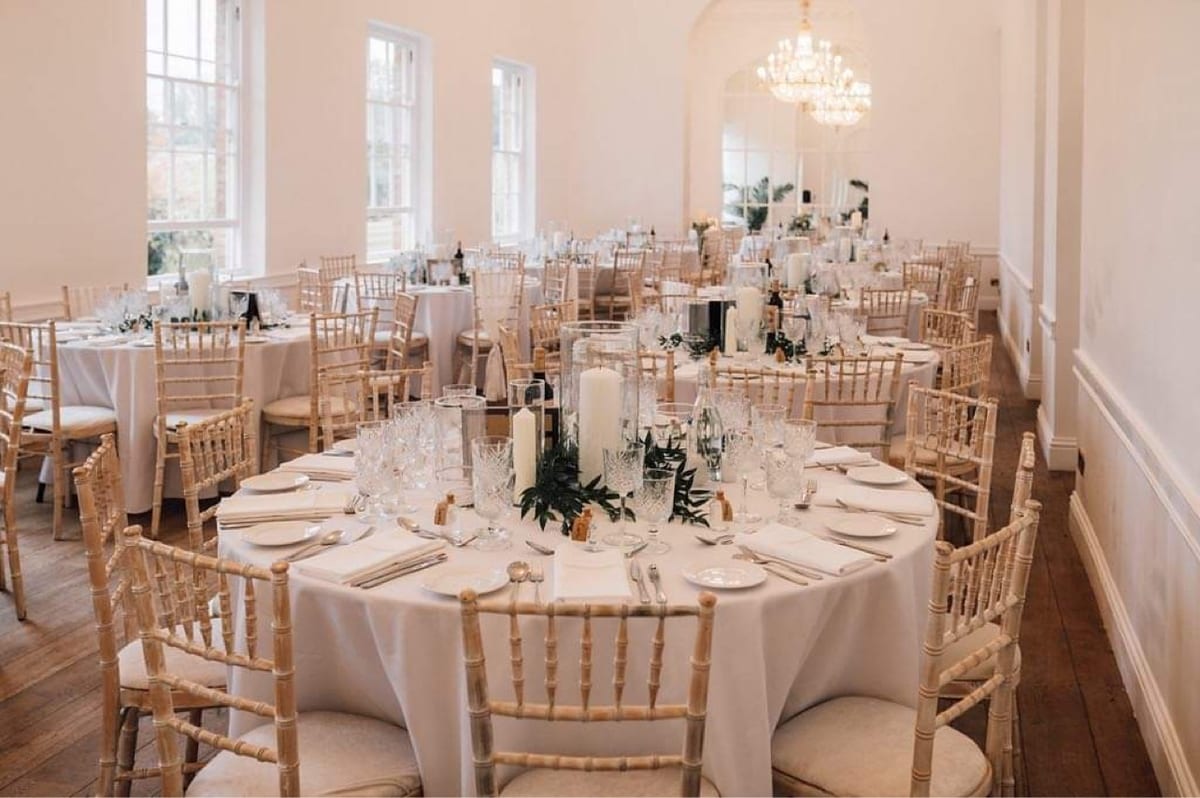 Round tables set with gold chairs, candles and low arrangements of white flowers.