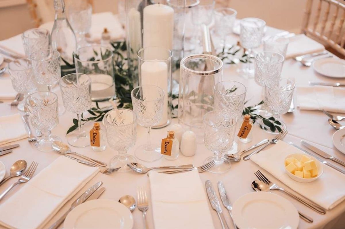 Close view of a place setting with candles, foliage and a name card.