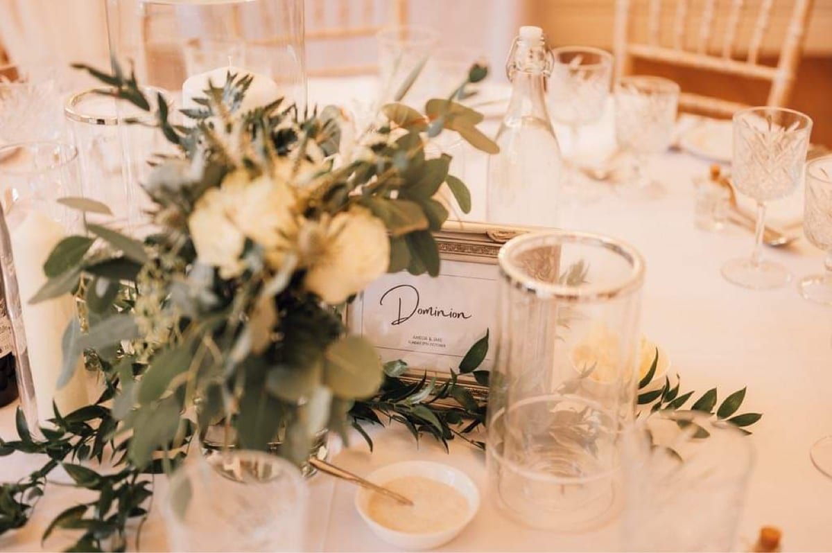 Low table centrepiece of white roses and foliage between pillar candles.