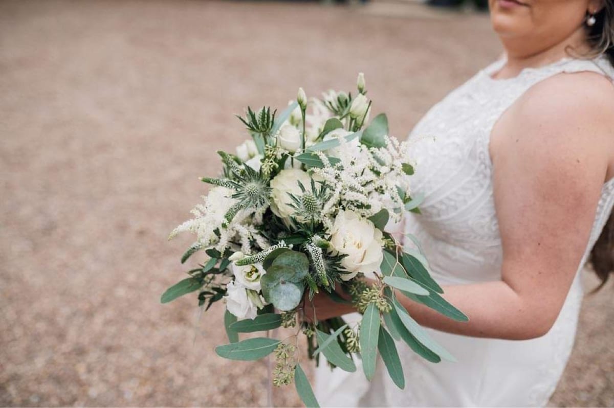 Bride holding a bouquet of white roses, foliage and trailing greenery.