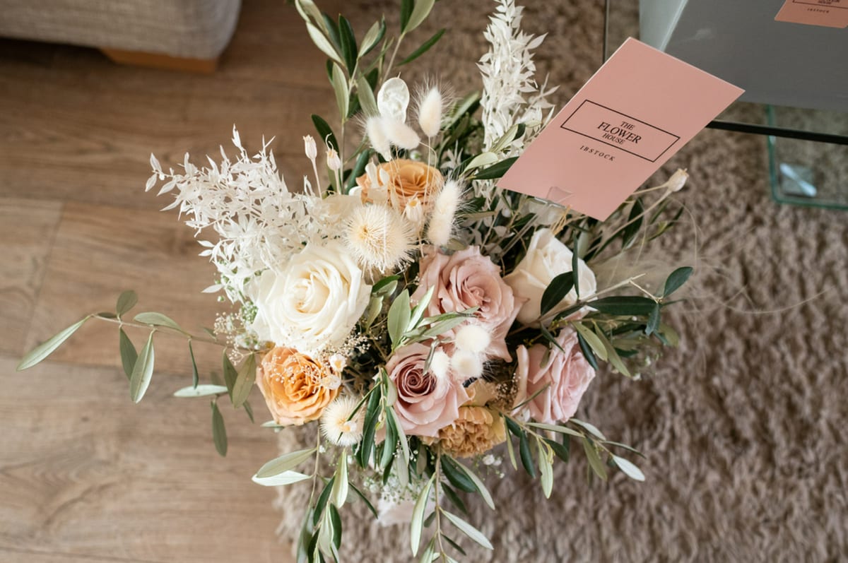 Bouquet of peach and cream roses with olive foliage, photographed from above beside a card.
