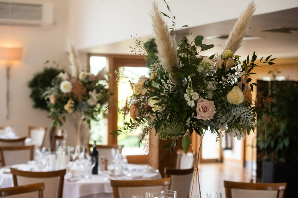 Tall pedestal arrangements of peach and cream flowers in a barn reception room.