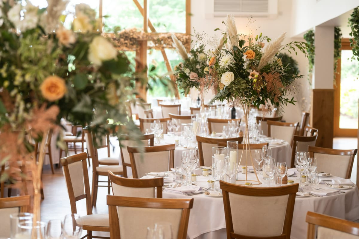Reception room with tall arrangements of dried grasses, roses and foliage above set tables.