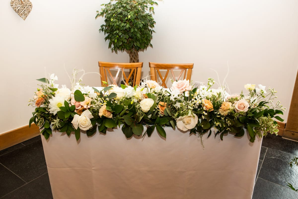 Top table garland of cream and peach roses with foliage running along the table edge.