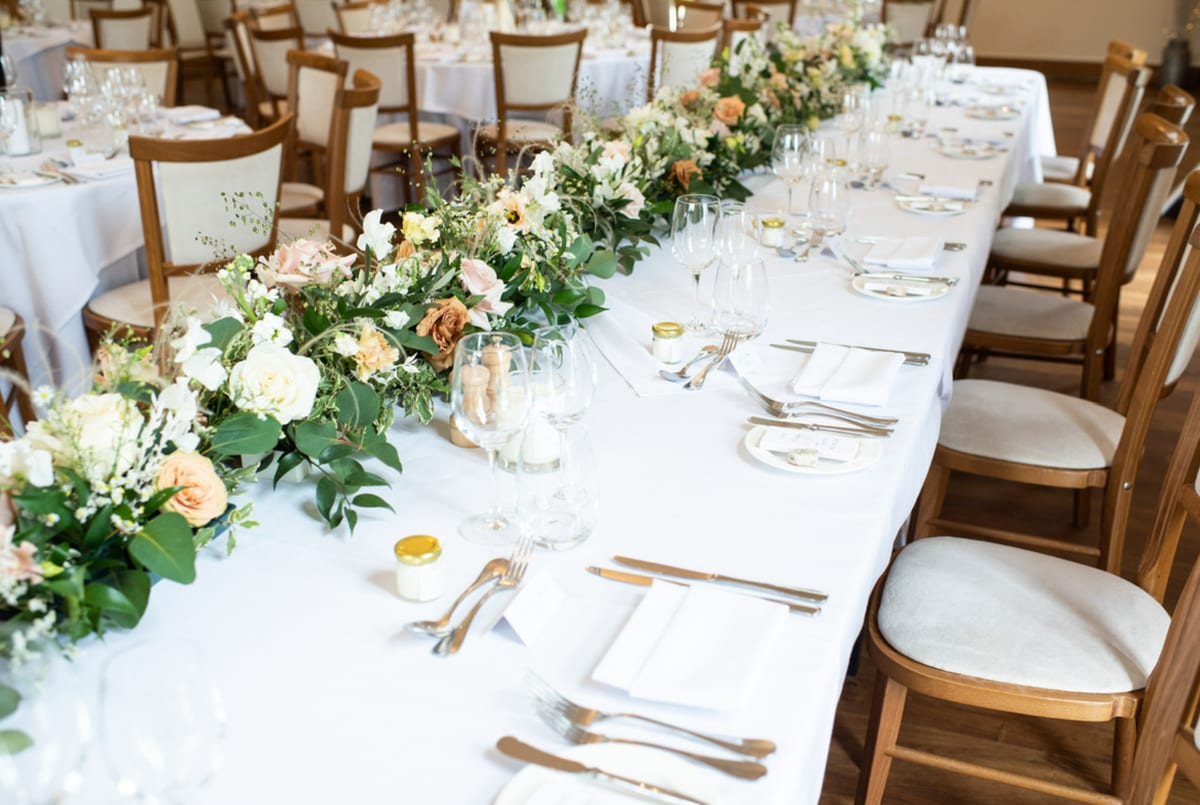 Long table dressed with a runner of foliage, cream roses and candles.