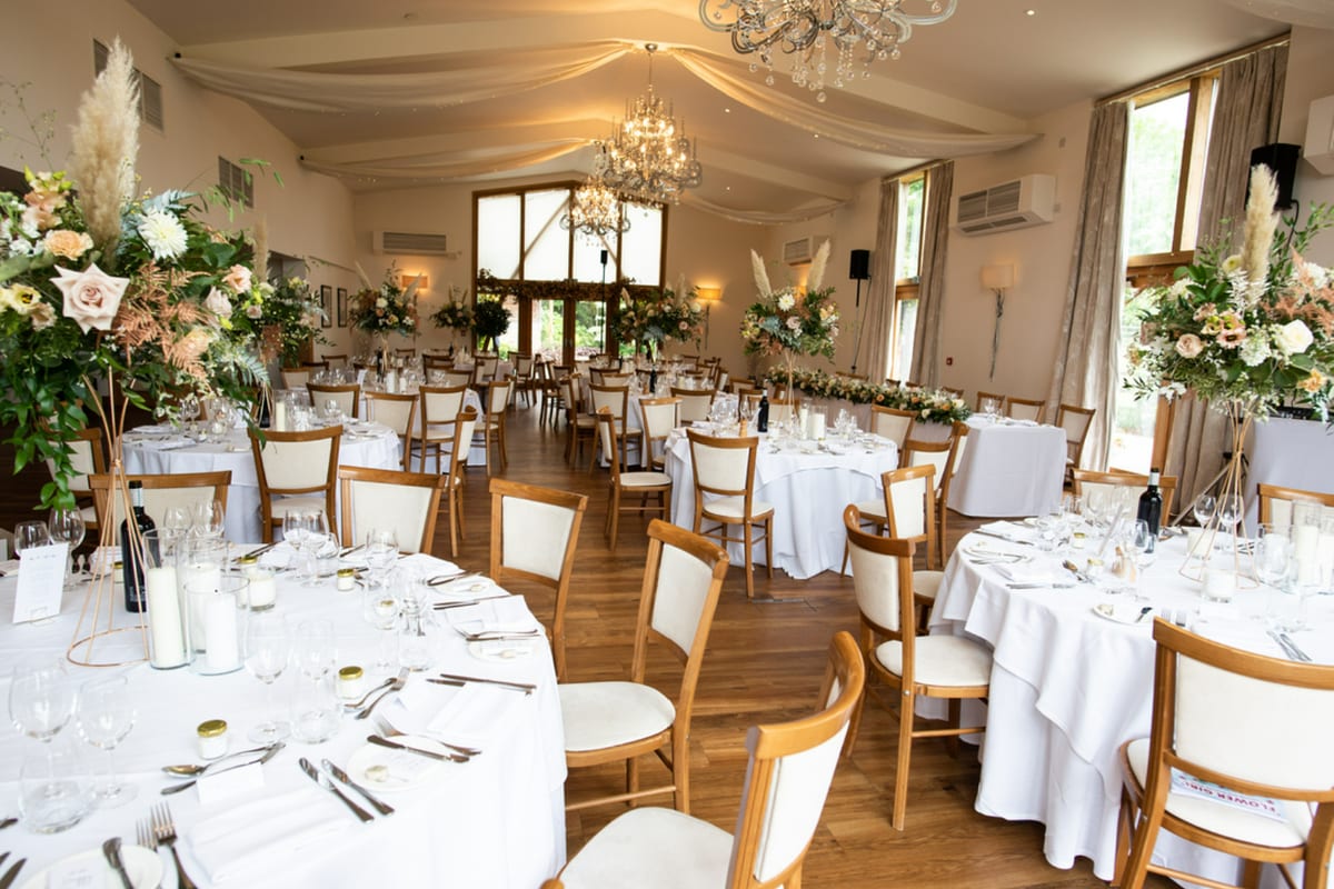 Barn reception room set for the wedding breakfast with round tables and tall arrangements.