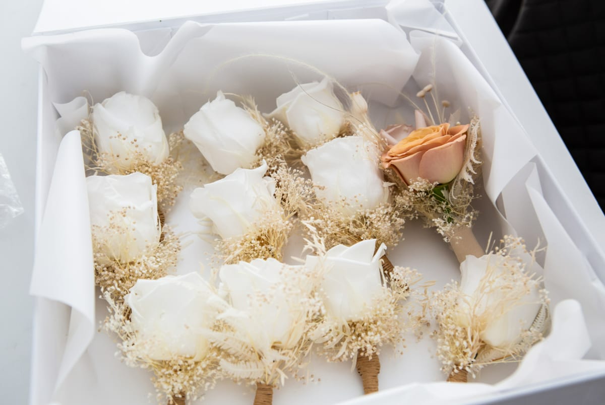 Boxed buttonholes of cream roses, dried grasses and fine white filler flowers.