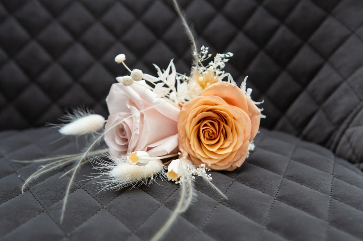 Buttonhole of a peach rose with dried grasses and fine white filler flowers.